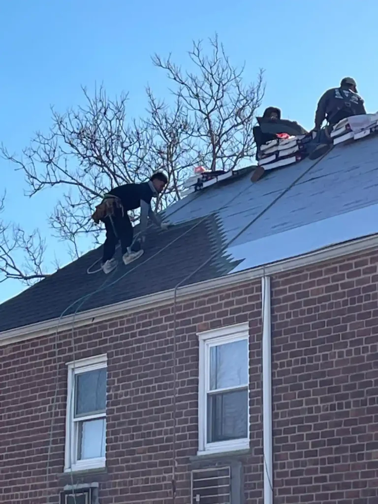 Workers performing the best roof replacement in Bronx NY on a brick house, showcasing professional roofing services by Alliance Construction NY under clear blue skies.